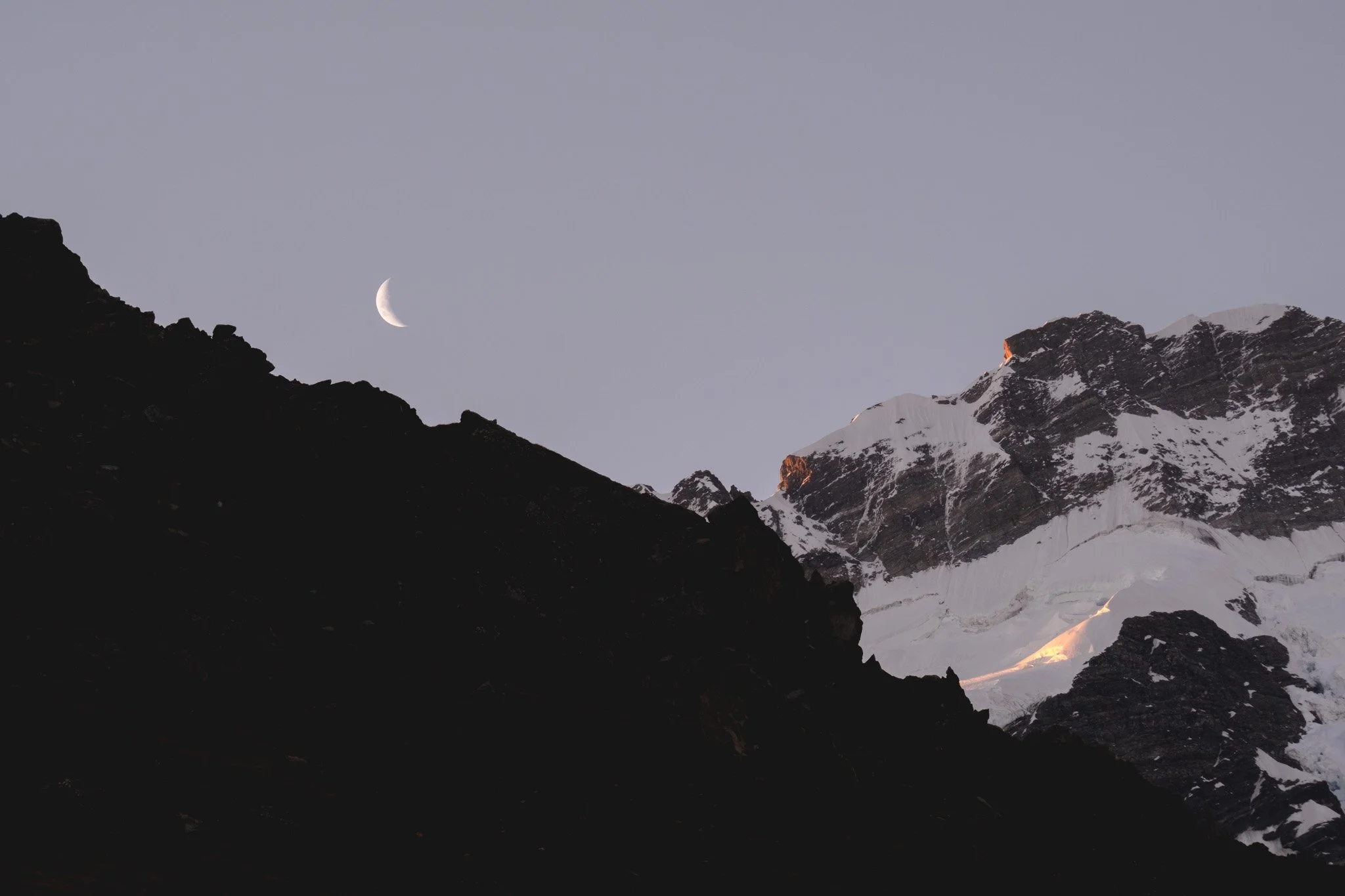 Experience the stunning beauty of nature in this captivating photograph of a crescent moon setting behind the silhouetted mountain lines in Mount Cook National Park. The serene and tranquil atmosphere of the image creates a sense of wonder and awe, h