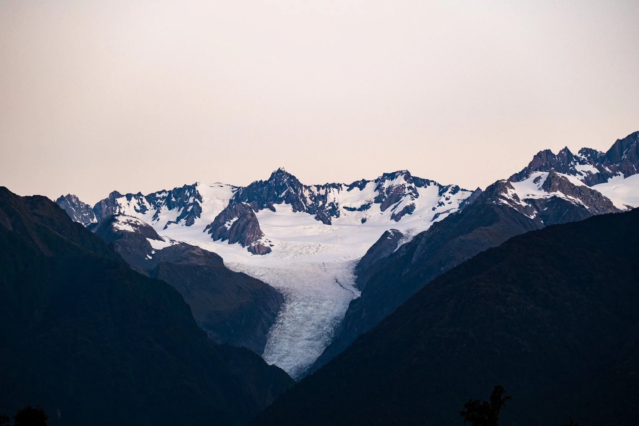 Fox Glacier in New Zealand during summer, starkly contrasted after sunset for a dramatic effect. A stunning and captivating image of the glacier's rugged beauty.