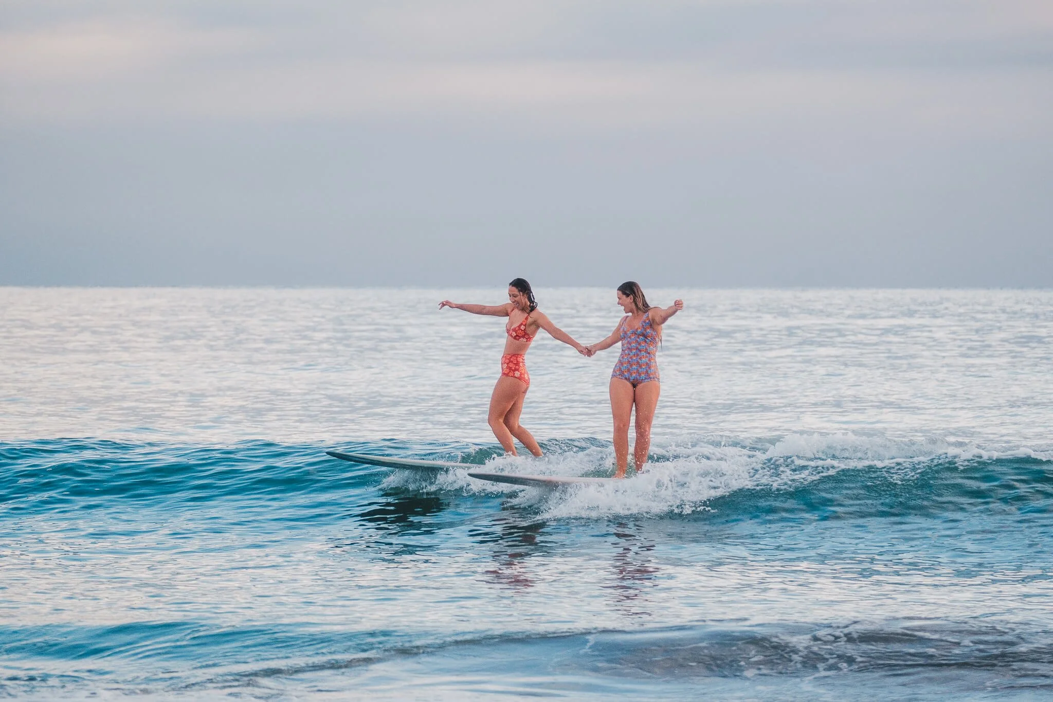 Surf lifestyle photo of two surf girls holding hands on a wave