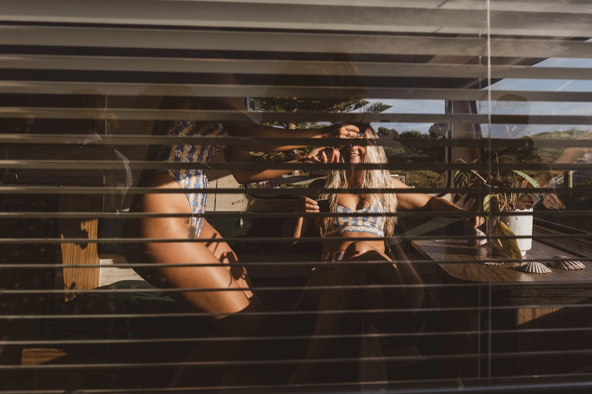 models inside vintage caravan captured through window blinds during Nostalgic Surf styled surf photography shoot natural lifestyle storytelling scene