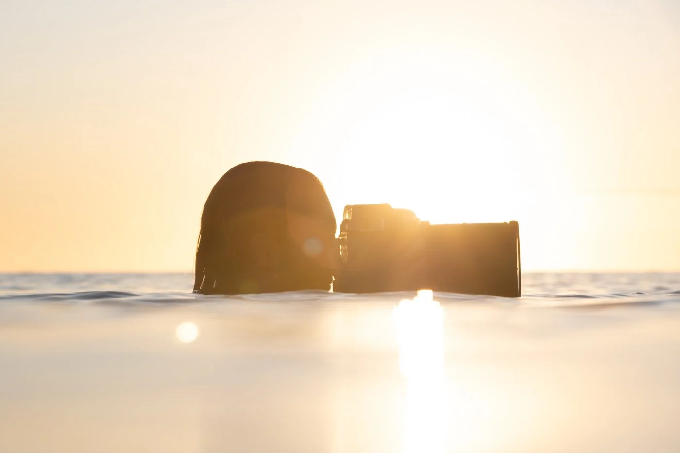 Surf photographer holding a camera in a surf photography water housing at ocean surface during sunrise
