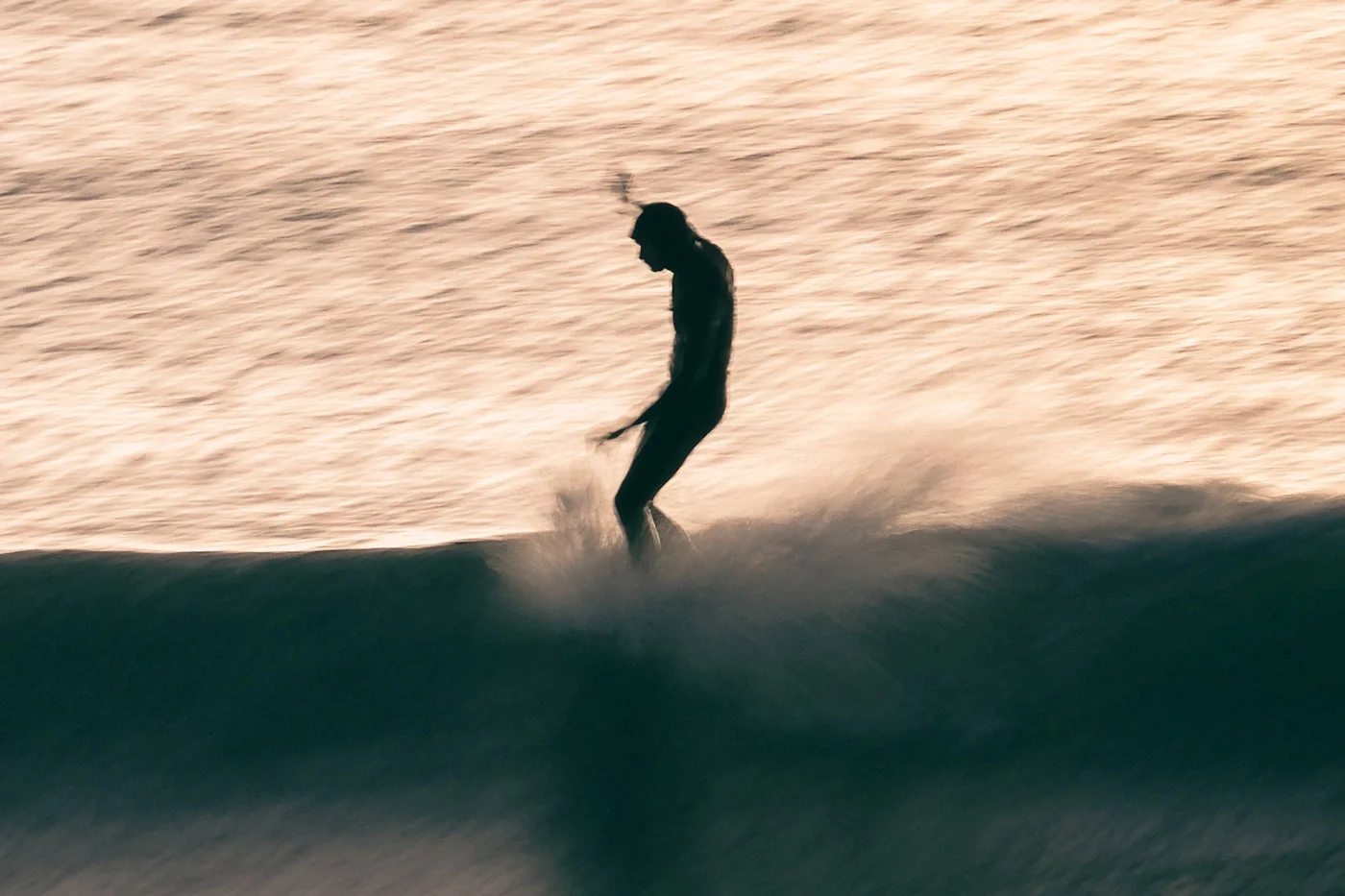 Surfer riding a small wave photographed from shore during golden hour surf photography session using slow shutter speed panning technique