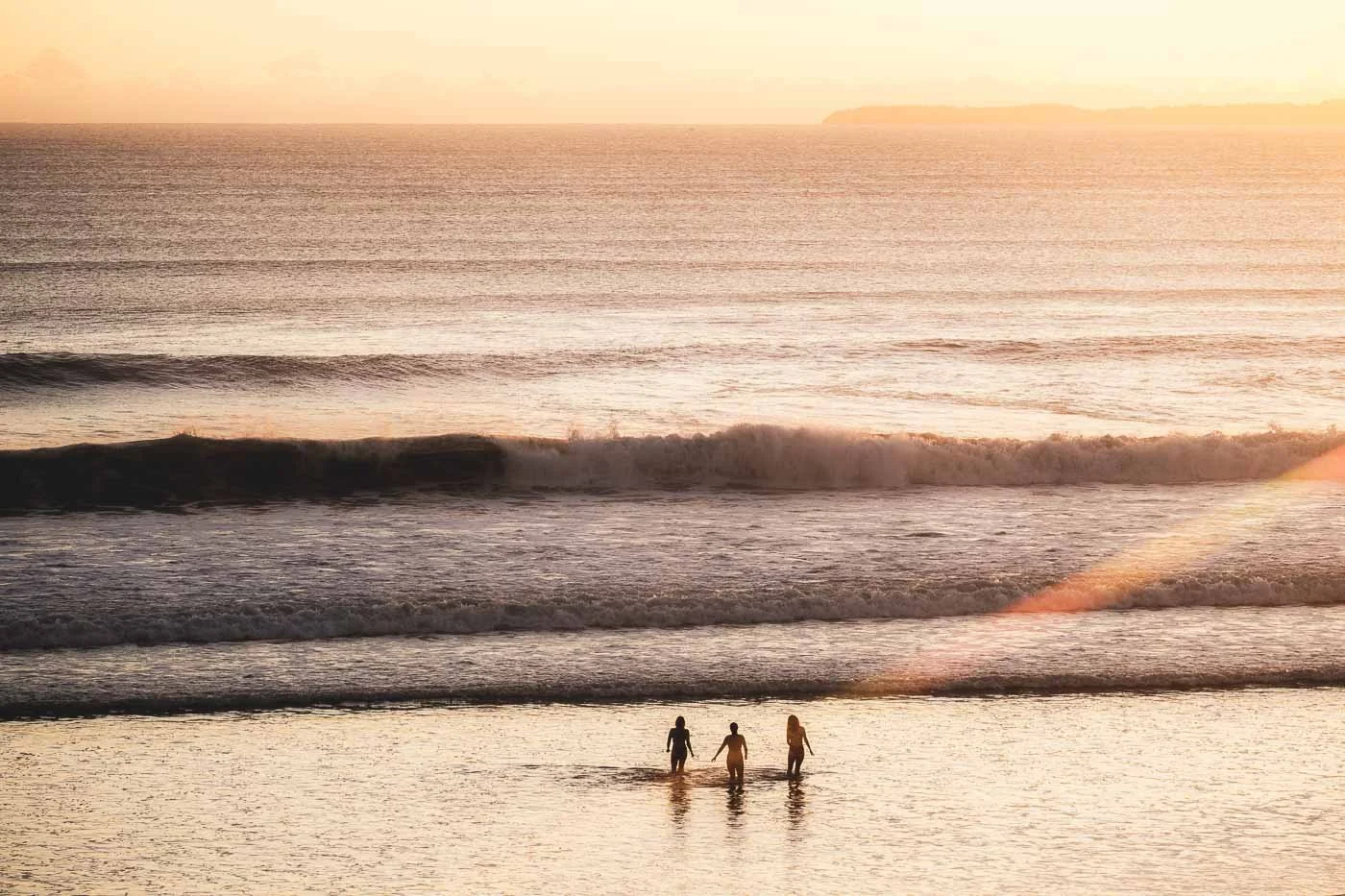 People standing in the ocean at sunrise at Mount Maunganui watching early morning light over the Pacific