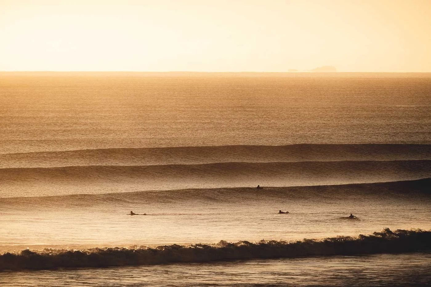 Surfers waiting beyond the break during sunrise at Mount Maunganui with layered golden ocean swell