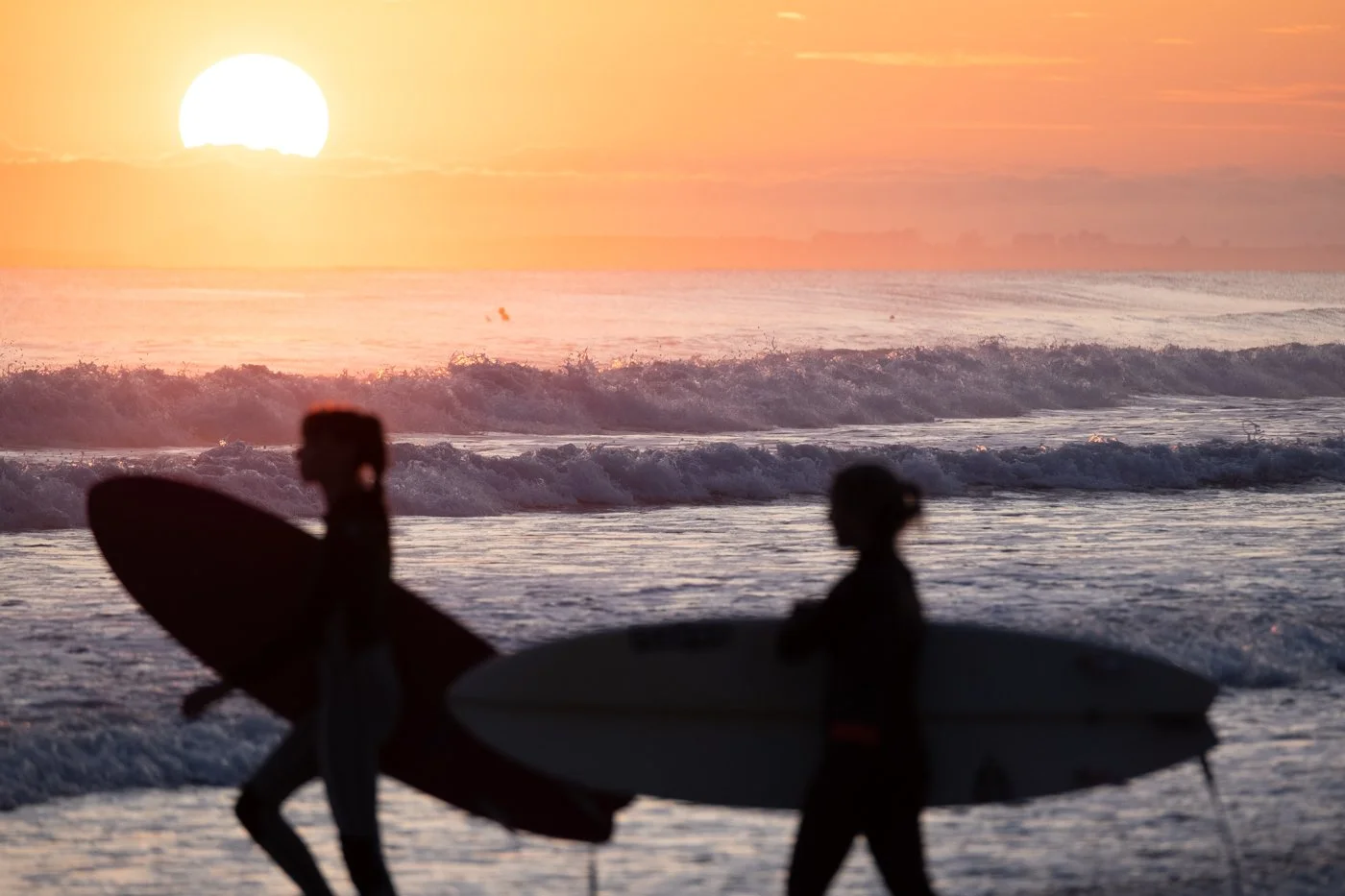 Surfers entering the water at sunrise at Mount Maunganui Beach with golden light on breaking waves