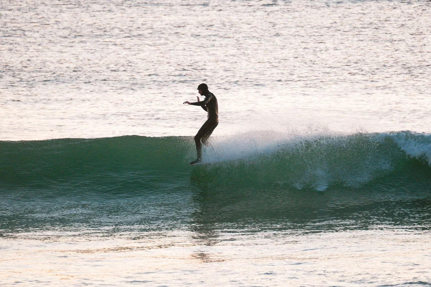 Surfer riding a small wave photographed from the shoreline with telephoto surf photography perspective