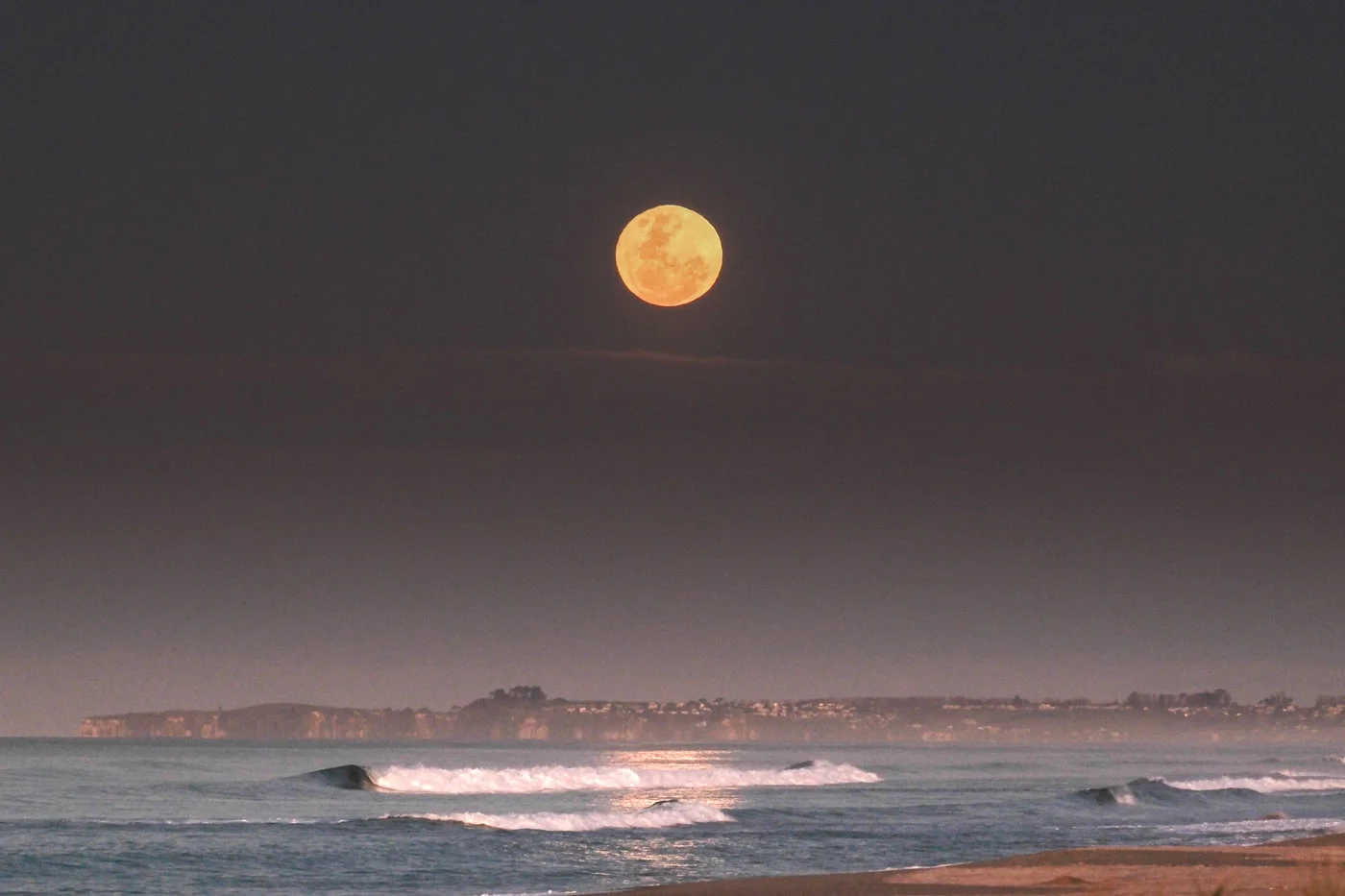 full moon rising above ocean horizon photographed with long focal length lens