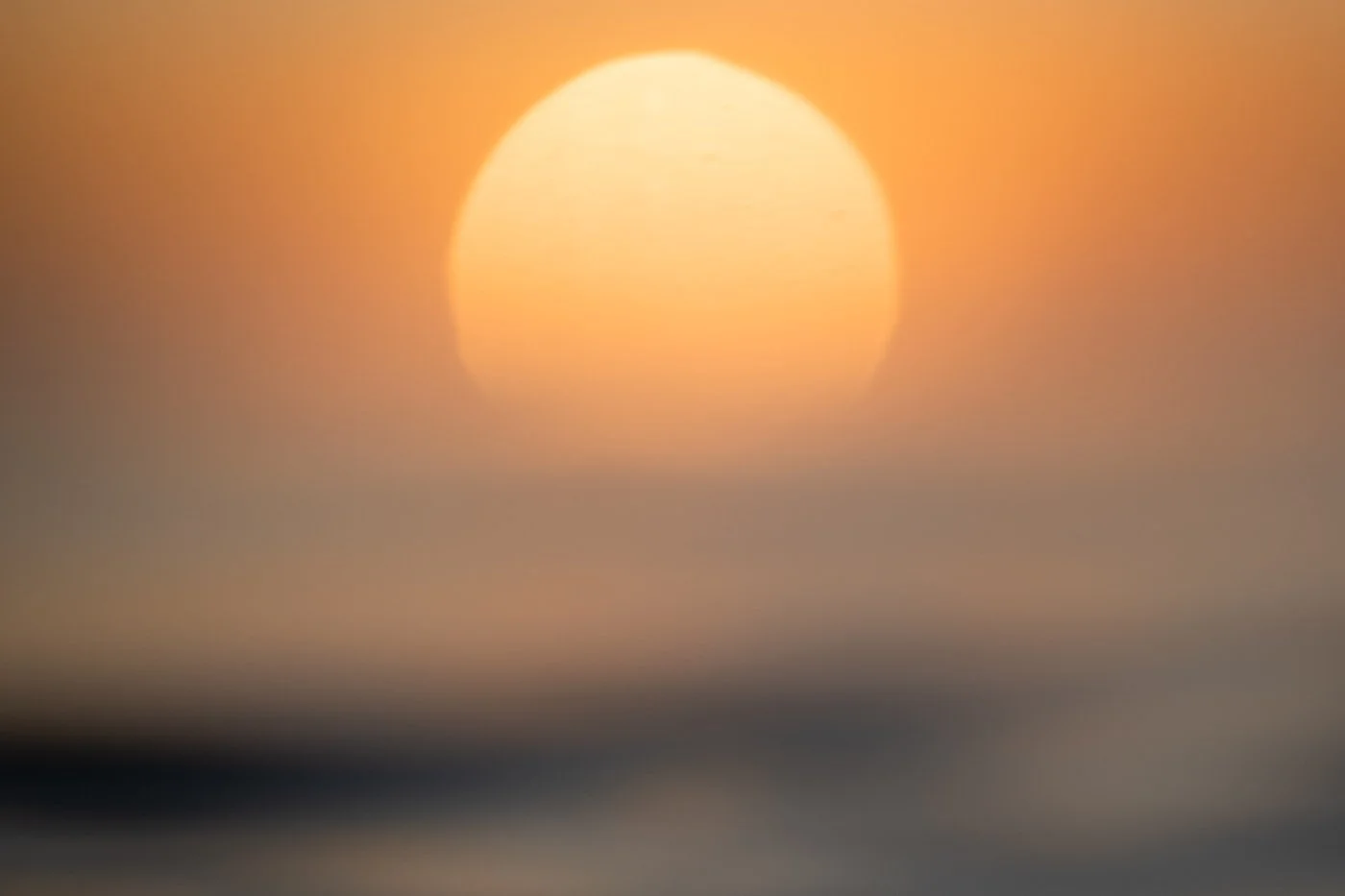 sun appearing large over ocean horizon showing compression effect in water photography