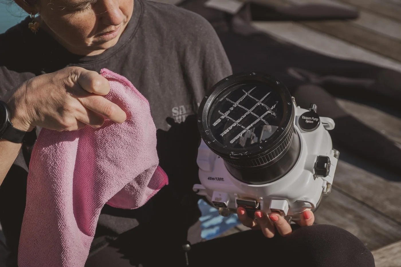 Photographer polishing surf wax from a waterproof camera housing flat port with a microfibre cloth.