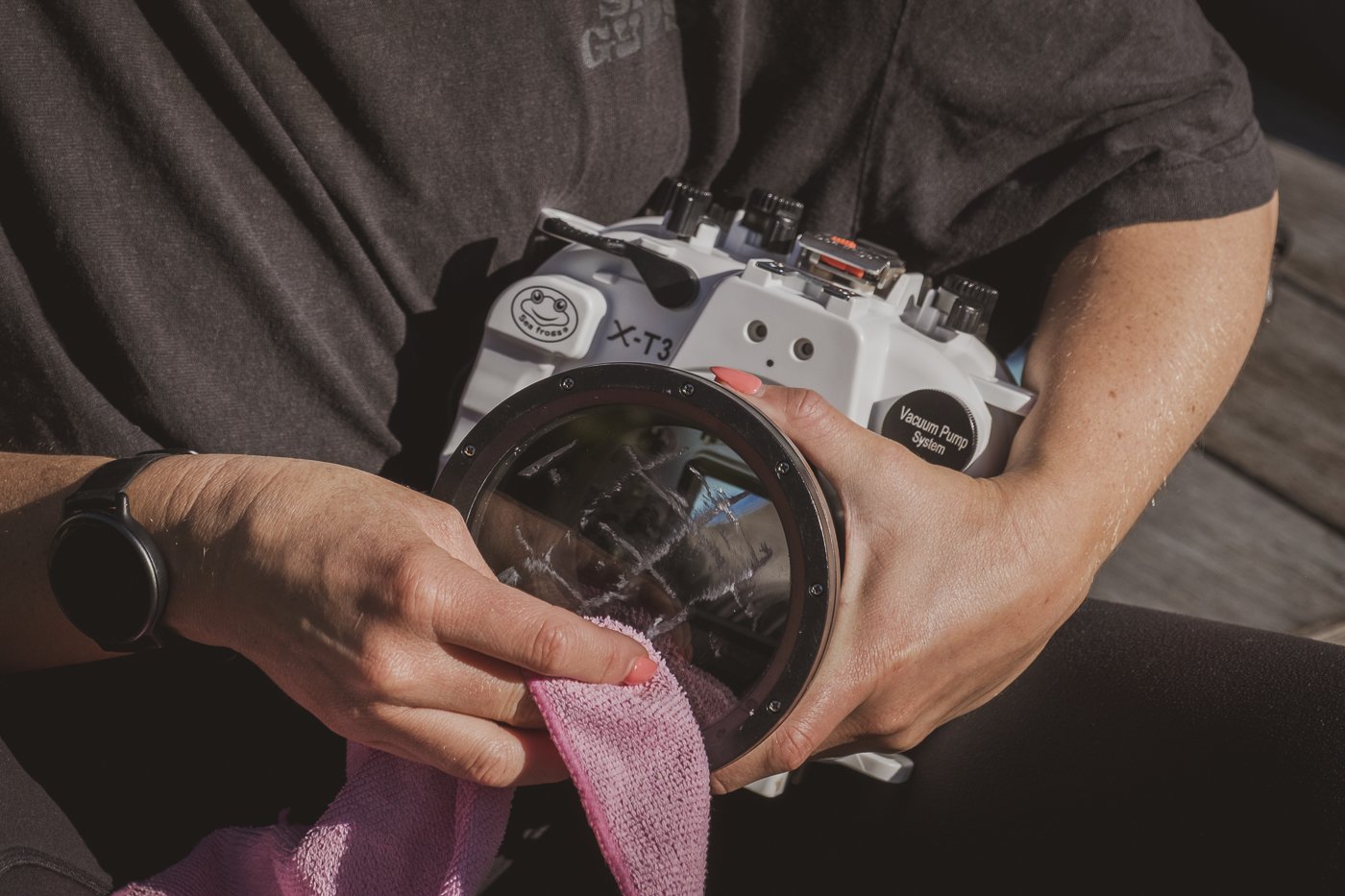 Microfibre cloth buffing a waterproof camera housing port to create a cleaner water-shedding surface.