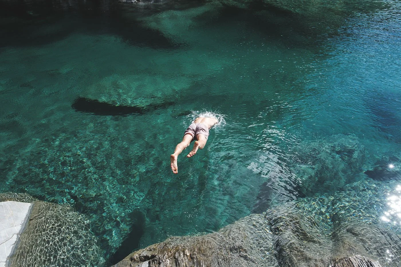 Swimmer diving into clear turquoise water at the Blue Pools near Wanaka in New Zealand.