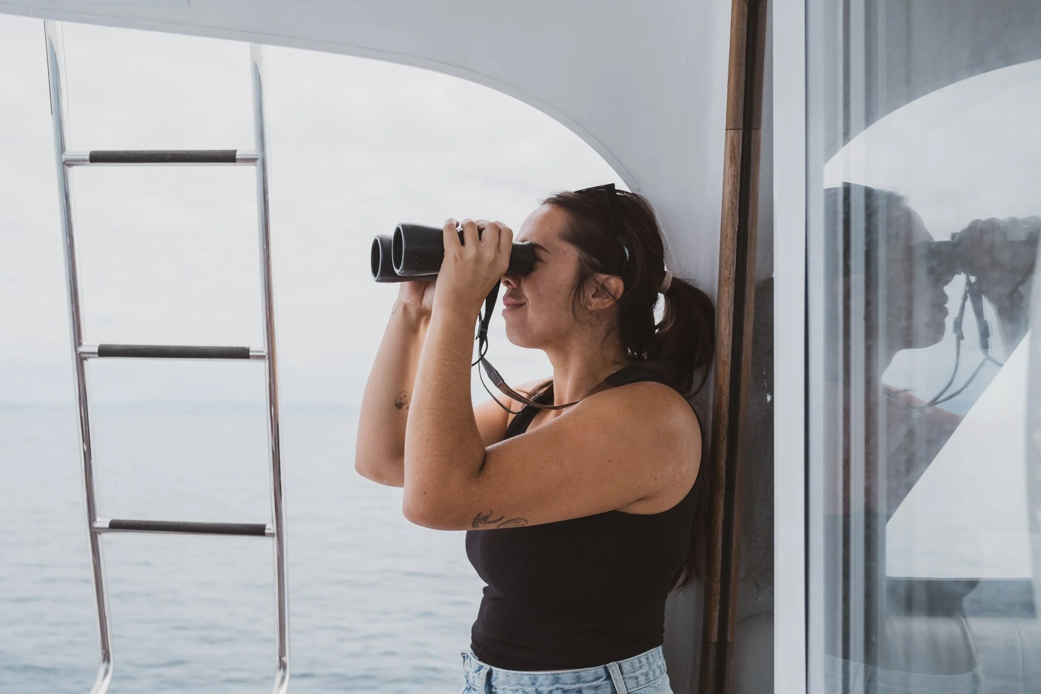 Woman looking through binoculars from a boat while searching for dolphins and marine wildlife at sea.