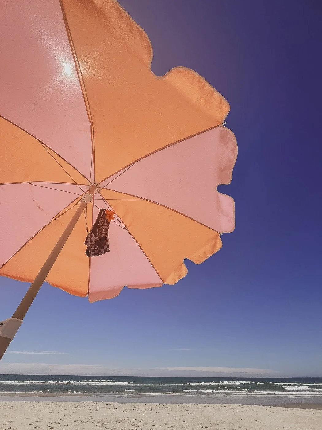 Looking up at a pink and orange beach umbrella against a clear blue summer sky.
