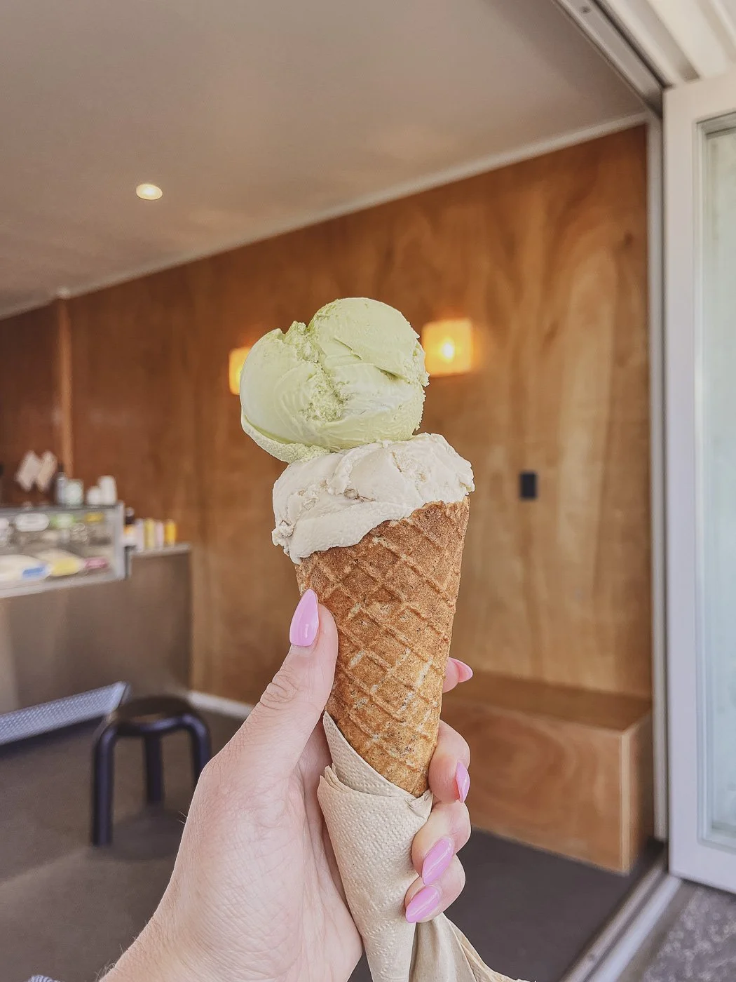 Two scoops of vegan ice cream in a waffle cone, held inside Sea People Ice Cream in Mount Maunganui.
