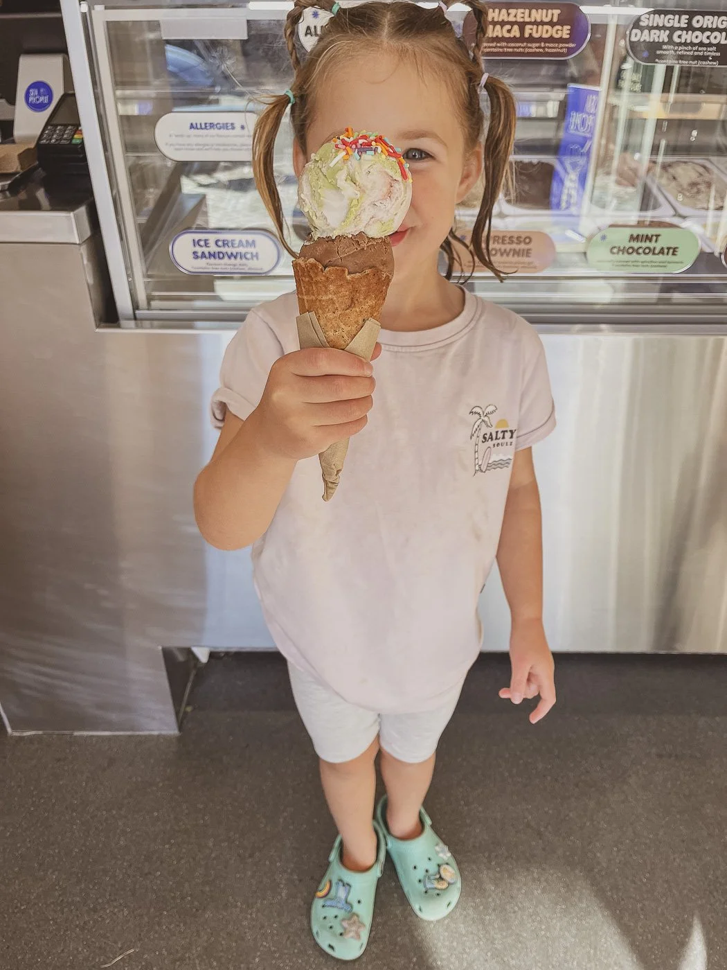 Young child holding an ice cream cone in front of the ice cream counter at Mount Maunganui.
