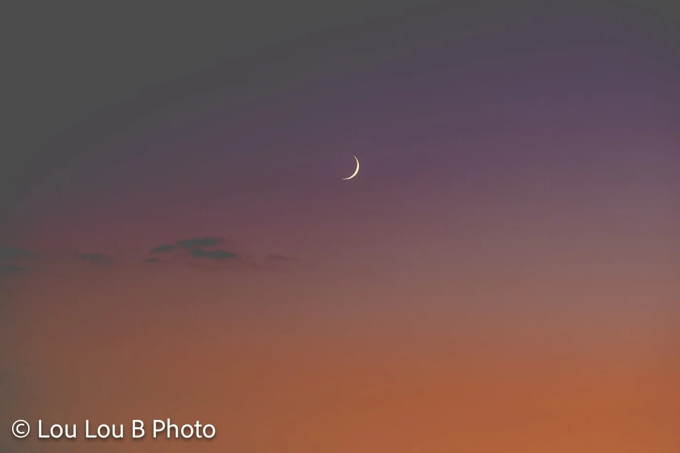Small crescent moon suspended in a gradient sky of lavender, pink and warm orange at dusk.