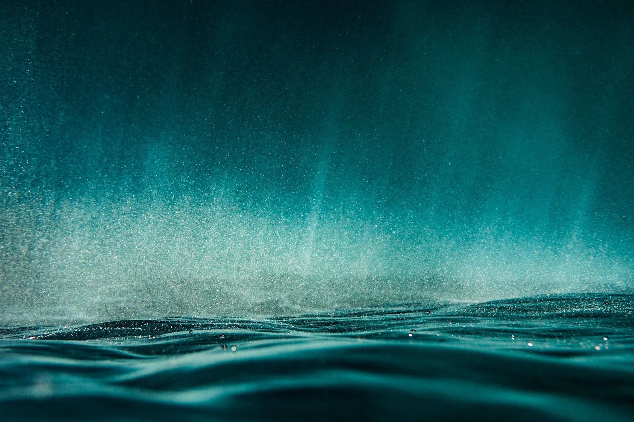 A photo of the rich turquoise underside surface of the ocean. The smooth and tranquil texture of the water creates a sense of serenity and calmness.
