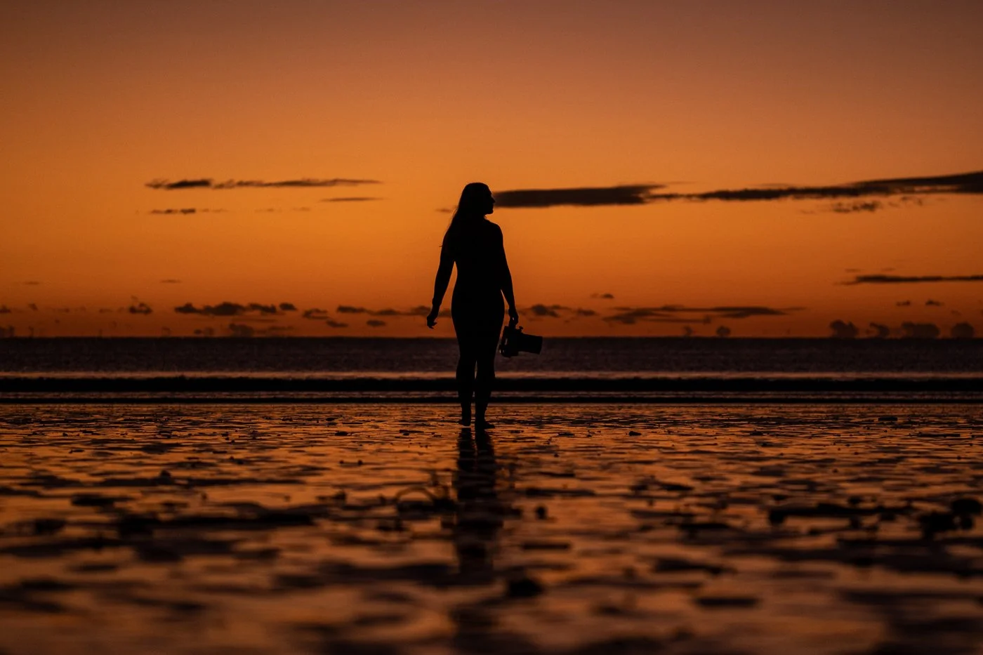 Silhouette of a surf photographer holding a waterproof camera housing while walking into the ocean at sunrise.