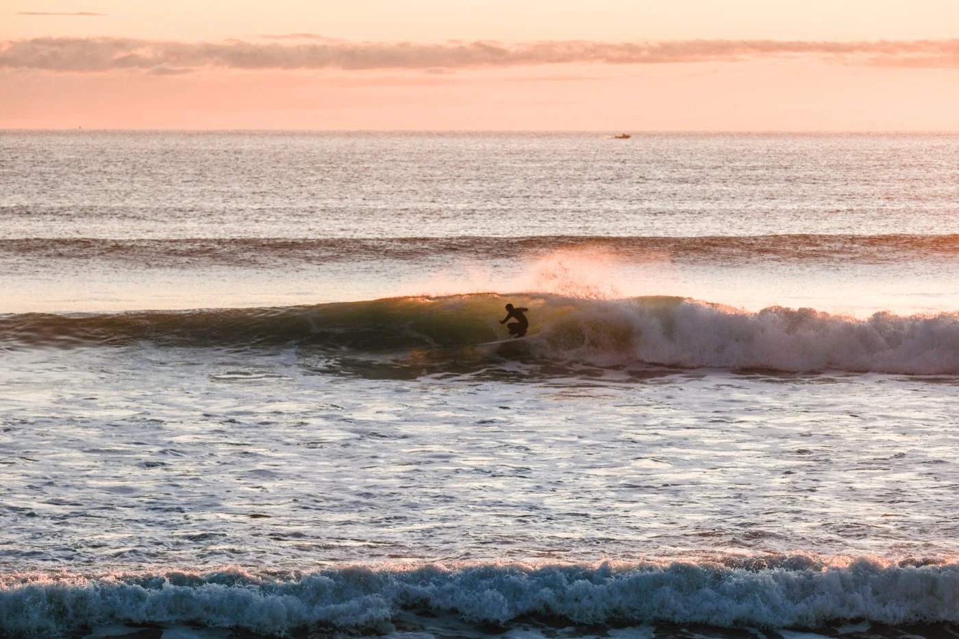 surfer riding small wave photographed from shoreline at 100mm focal length