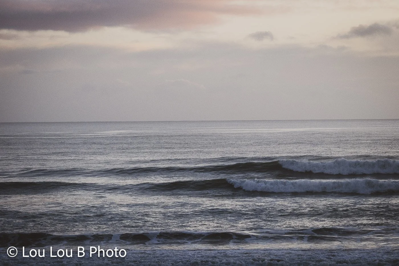 Layers of dark ocean swell rolling toward shore beneath a moody grey and muted pink sky.