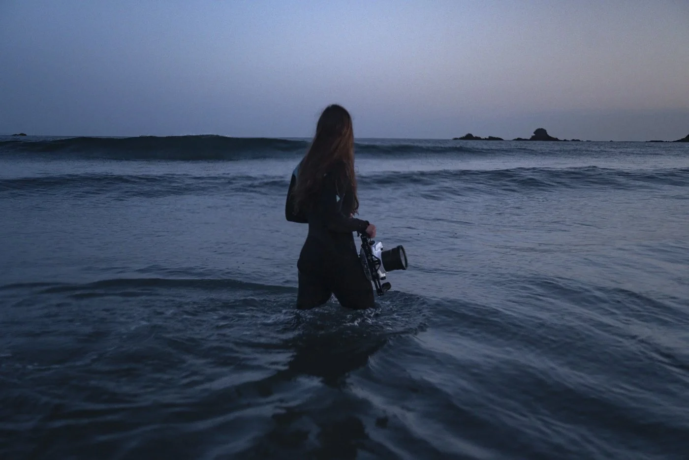 Female surf photographer entering the ocean with an underwater camera housing before an in-water surf photography session