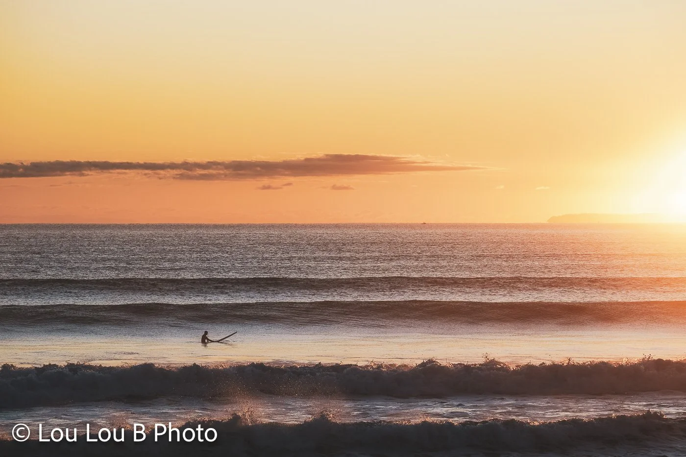 Surfer riding a breaking wave beneath a vivid orange sunrise over the ocean.