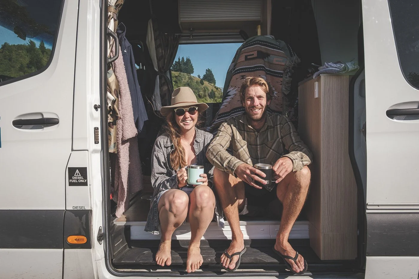 Couple sitting in the doorway of their rented campervan during a New Zealand road trip.