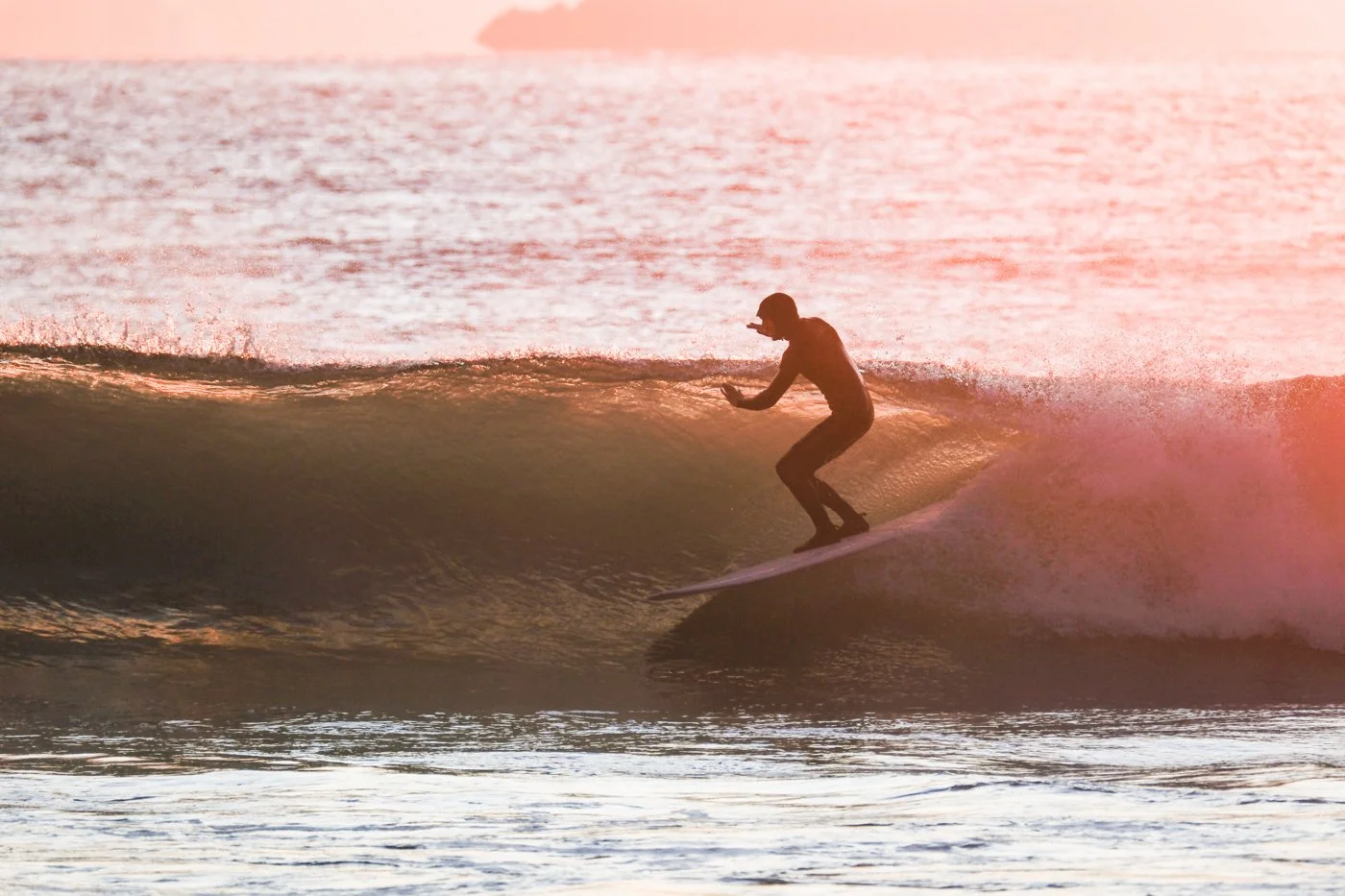 Surfer riding a wave at sunset photographed from the shoreline with backlit spray frozen using fast shutter speed