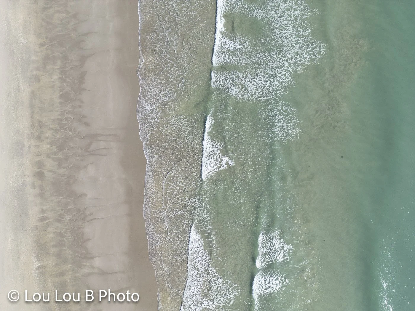 Aerial view of pale turquoise waves meeting a sandy beach.