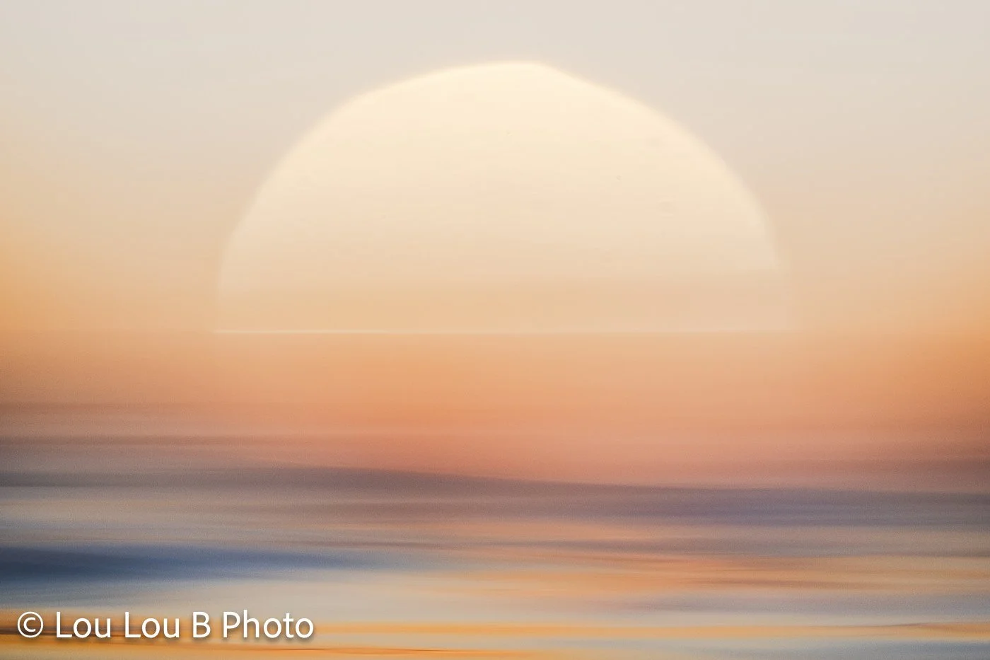 Large out-of-focus sun setting over a calm ocean in soft peach and champagne tones.