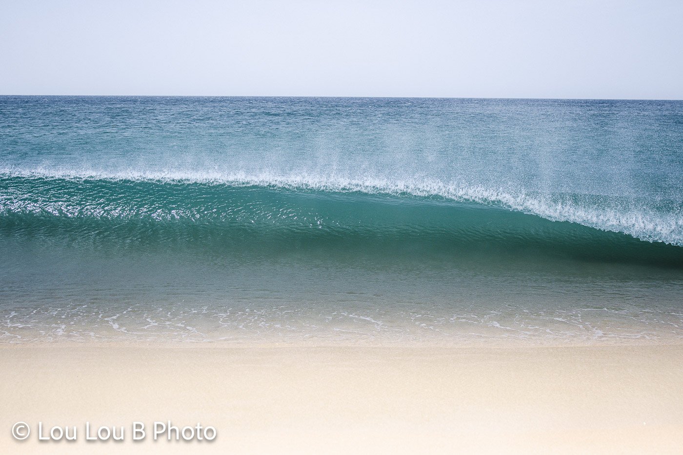 Turquoise breaking wave rolling towards a pale sandy beach.