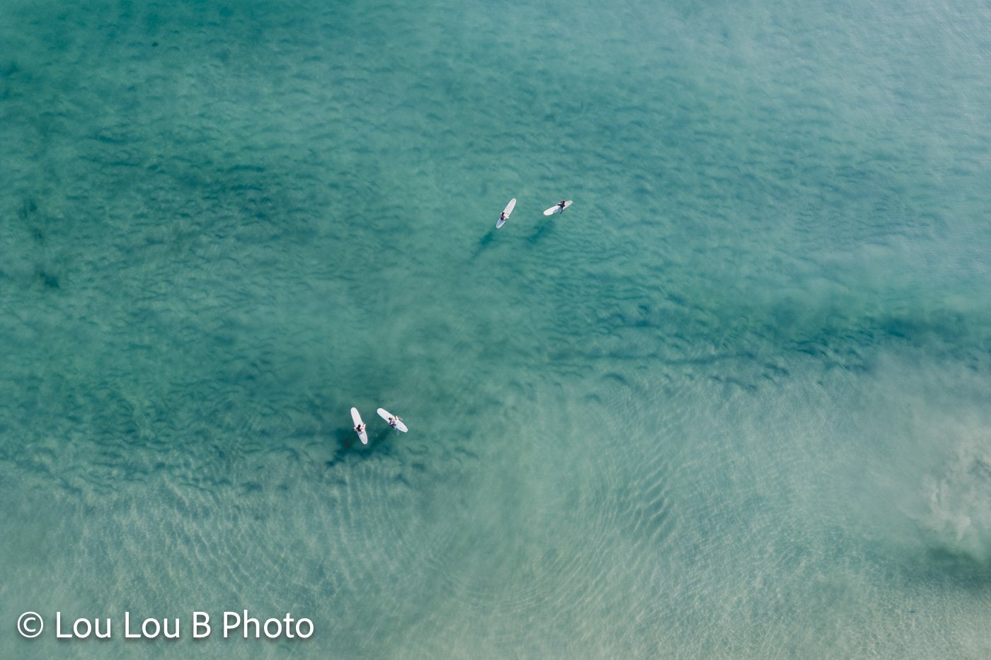 Aerial view of surfers in clear turquoise ocean water at Mount Maunganui