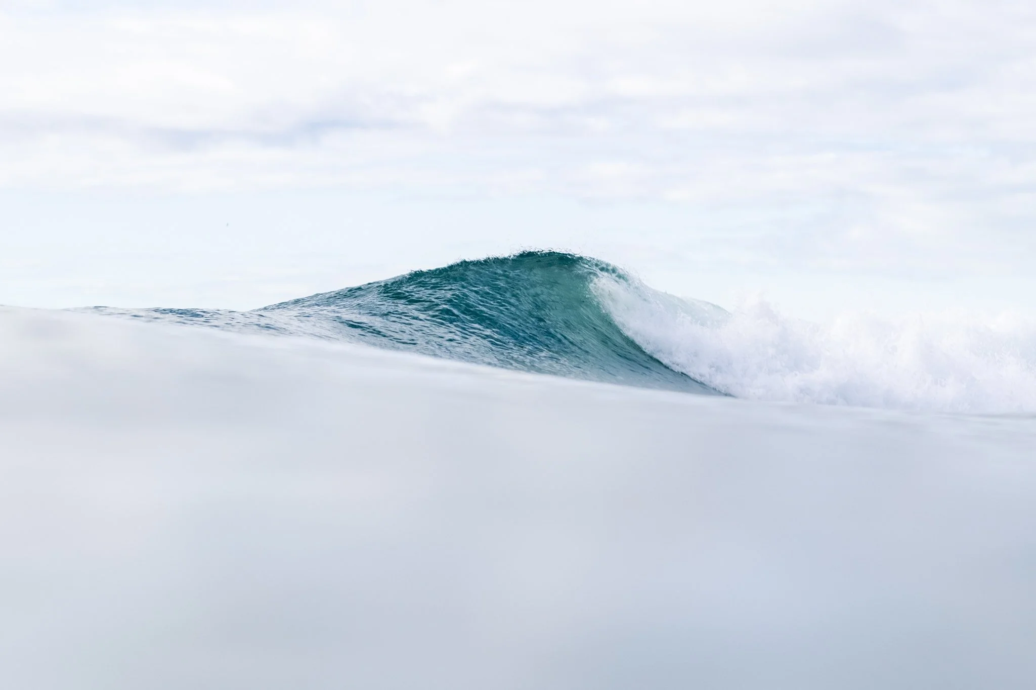 Turquoise ocean wave breaking through soft white sea spray.