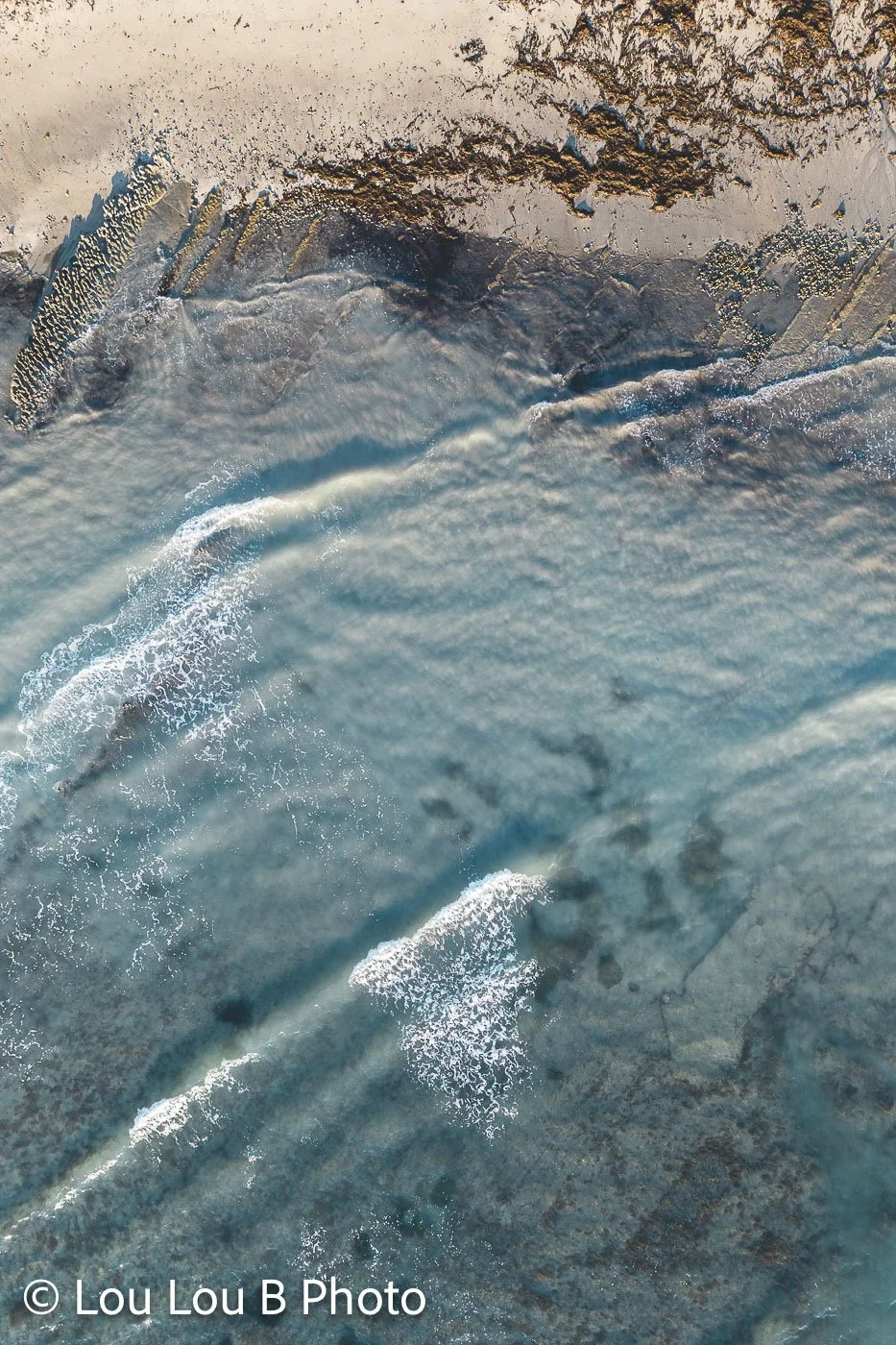 Aerial detail of clear turquoise water flowing over pale coastal rock in a coastal lagoon at Tatapouri Bay, Gisborne.