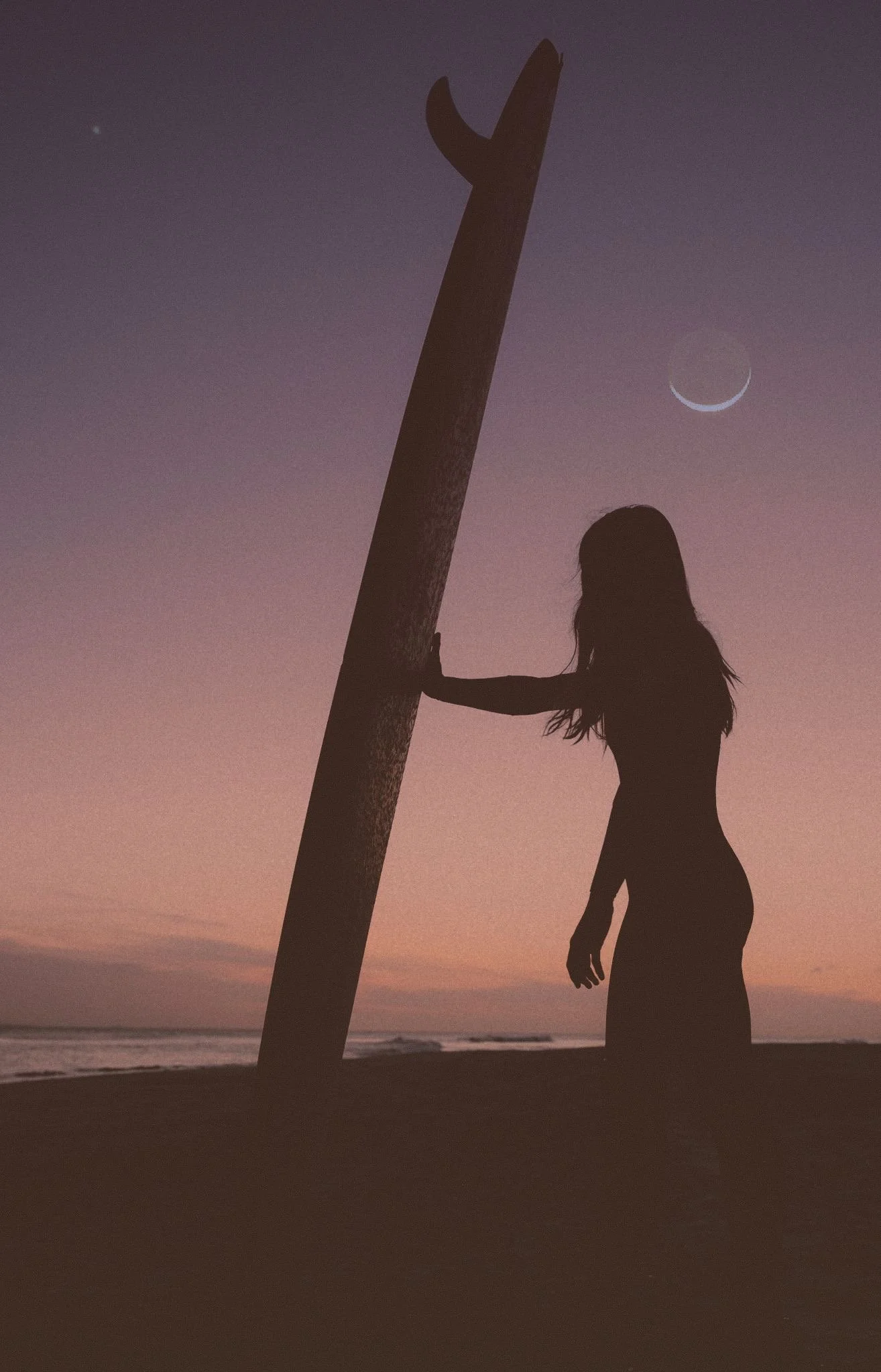 Female surfer and her board silhouetted against a crescent moon, featured on the cover of Betty Zine. A stunning surf lifestyle capture by Lou Lou B Photo.