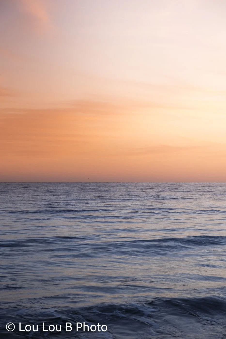 Gentle ocean swell beneath a vivid peach and orange sunset sky.
