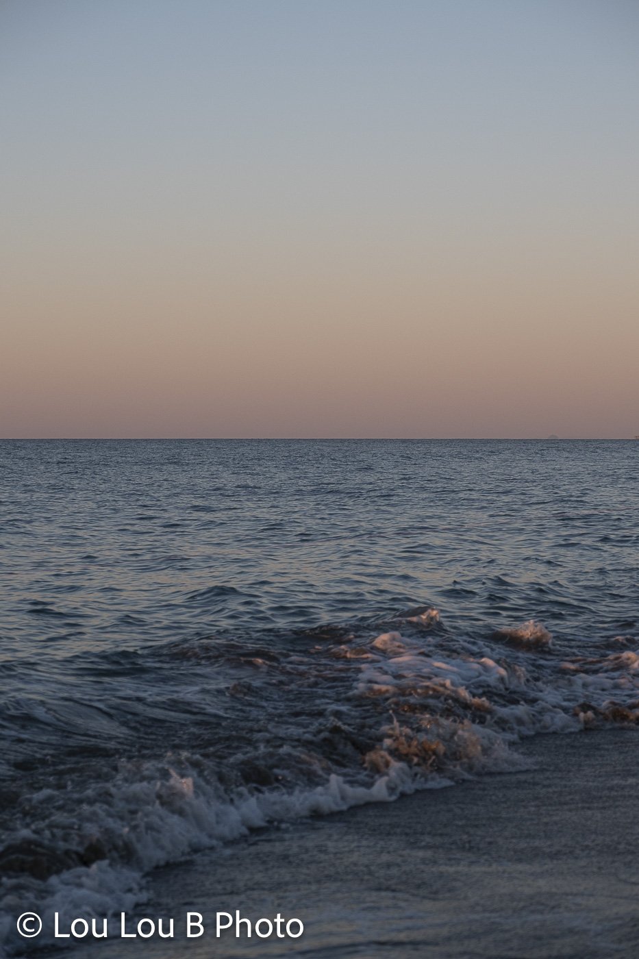 Textured ocean waves rolling toward shore beneath a minimal blue and peach horizon.