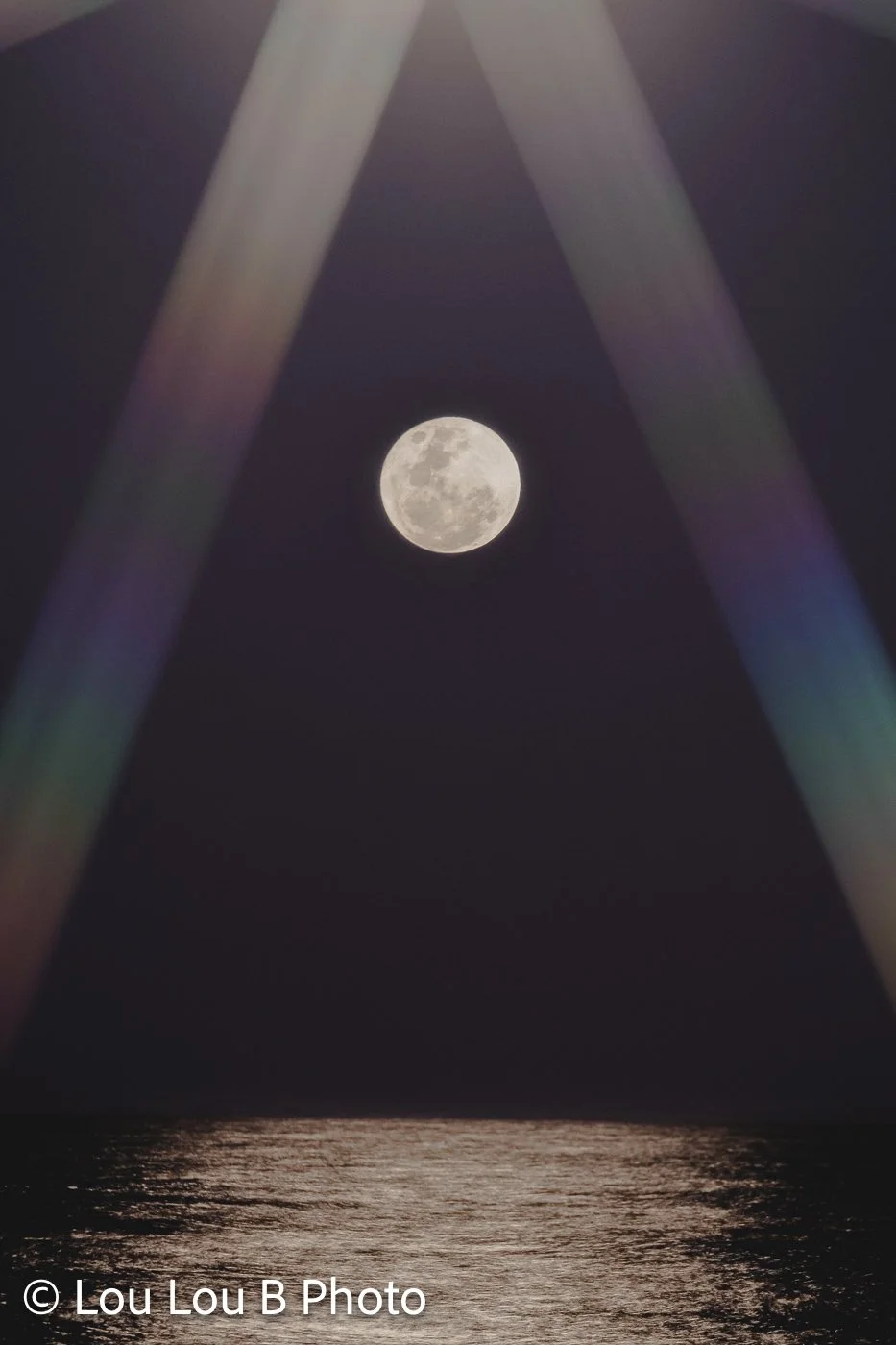 Full moon above the ocean framed by abstract beams of soft purple and blue light.
