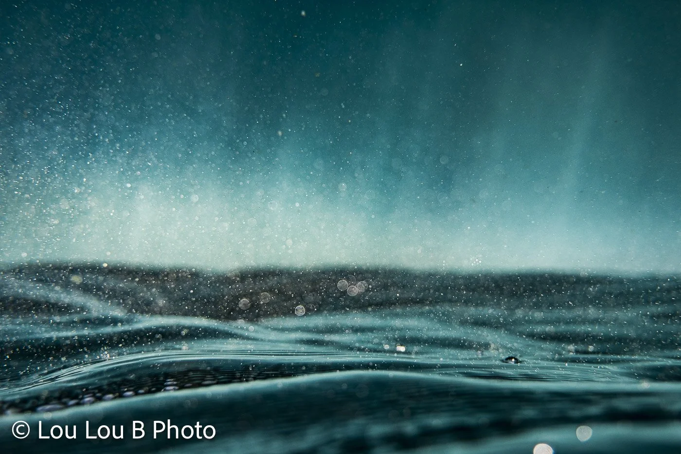 In-water view of deep turquoise ocean with sea spray and water droplets.
