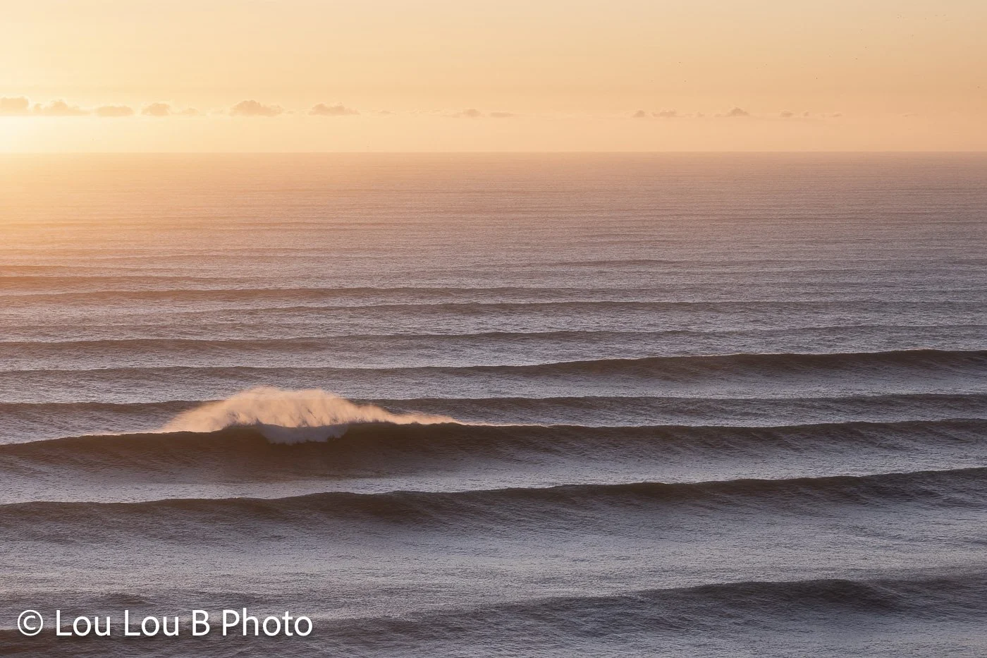 Parallel lines of ocean swell glowing beneath a warm peach and golden horizon.