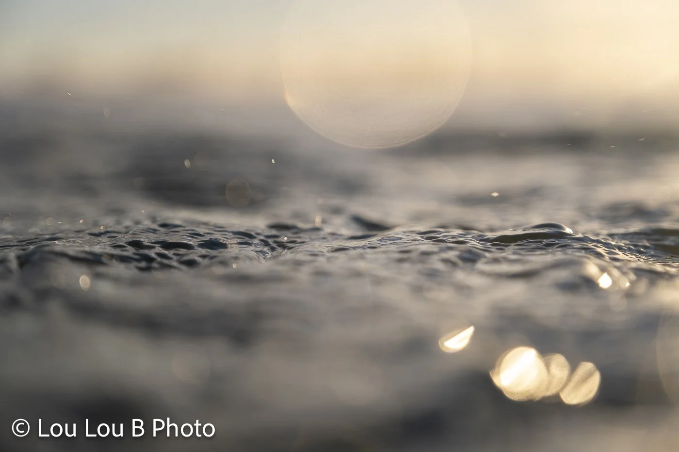 Low water-level view of gentle ocean ripples sparkling in soft golden light.