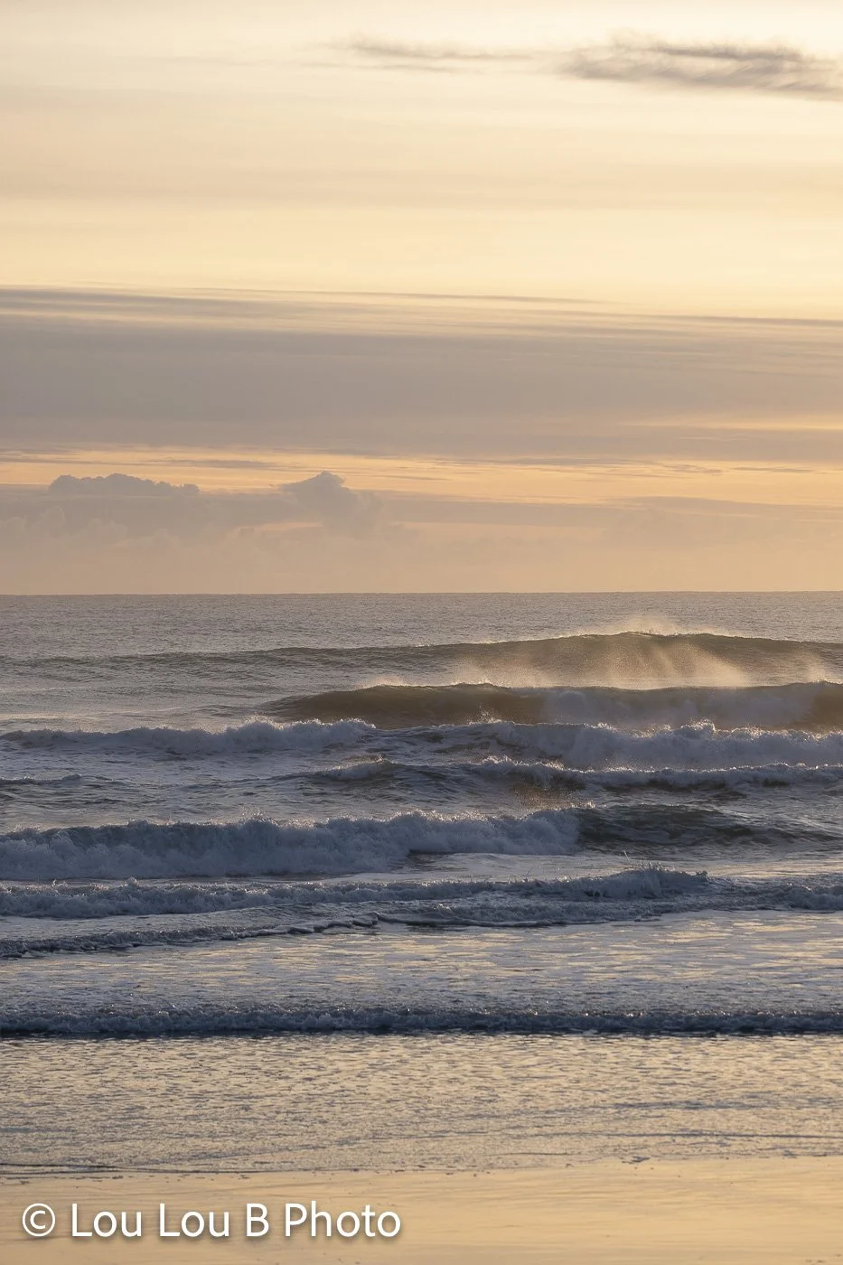 Breaking ocean waves glowing in warm evening light with hazy mountains on the horizon.