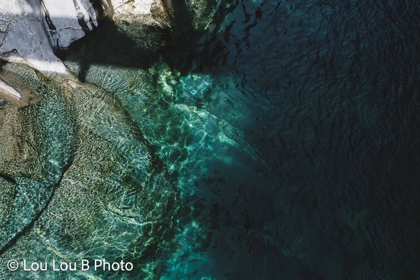 Aerial view of clear emerald and turquoise water surrounding coastal rock formations.