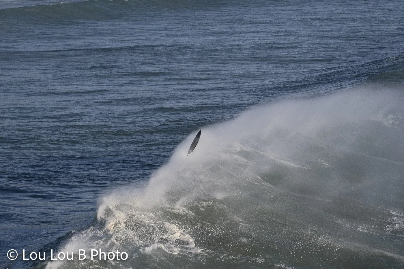 Large ocean wave exploding into whitewater with strong offshore spray blowing from the crest with tiny surfboard flying in the air.