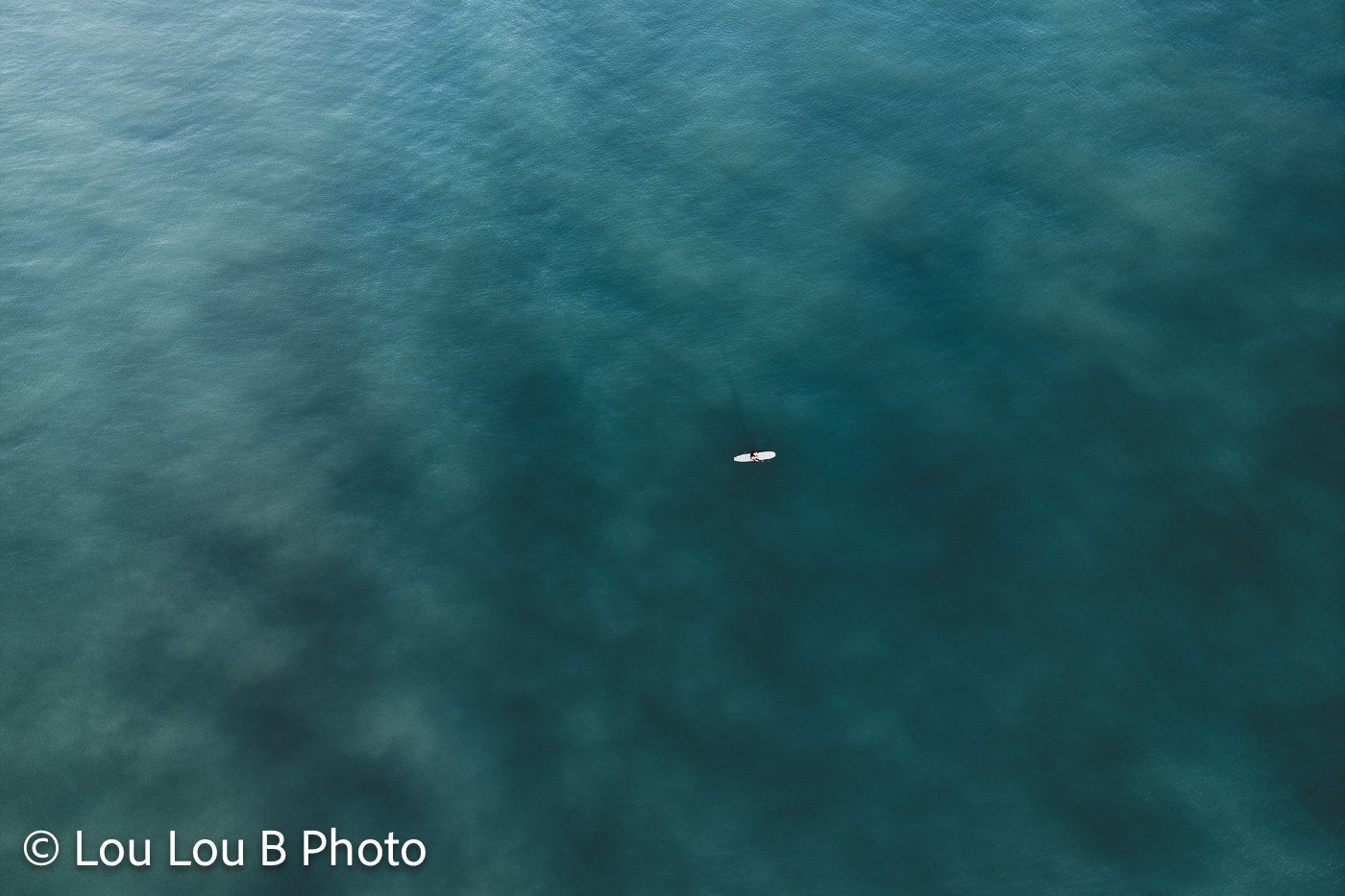 Aerial view of deep turquoise ocean water with a lone surfer surrounded by open sea.
