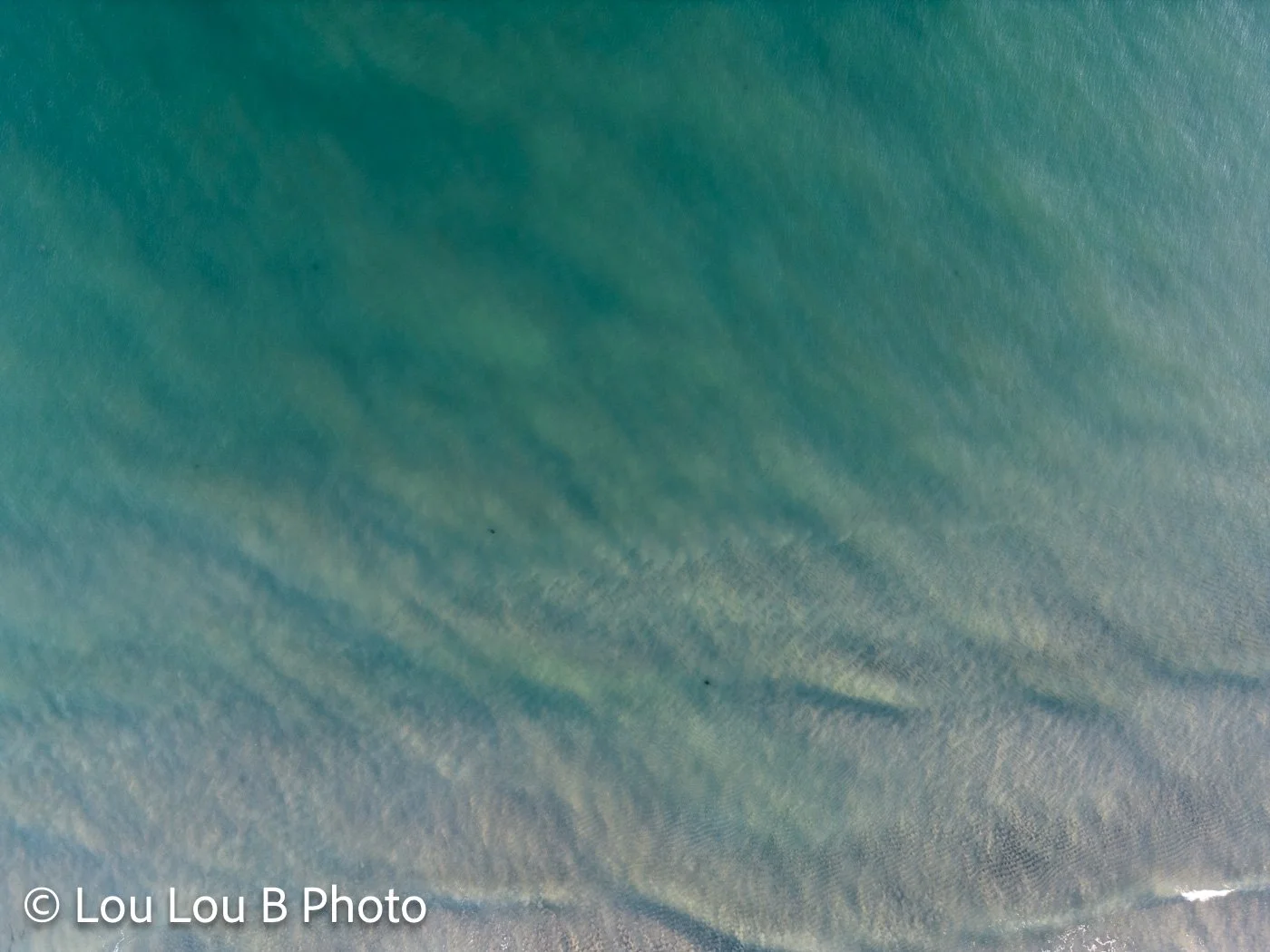 Aerial view of turquoise ocean textures and sand beneath the water at Mount Maunganui