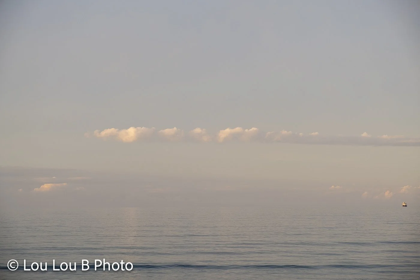 Calm ocean beneath a hazy sky with small clouds glowing in soft champagne light.
