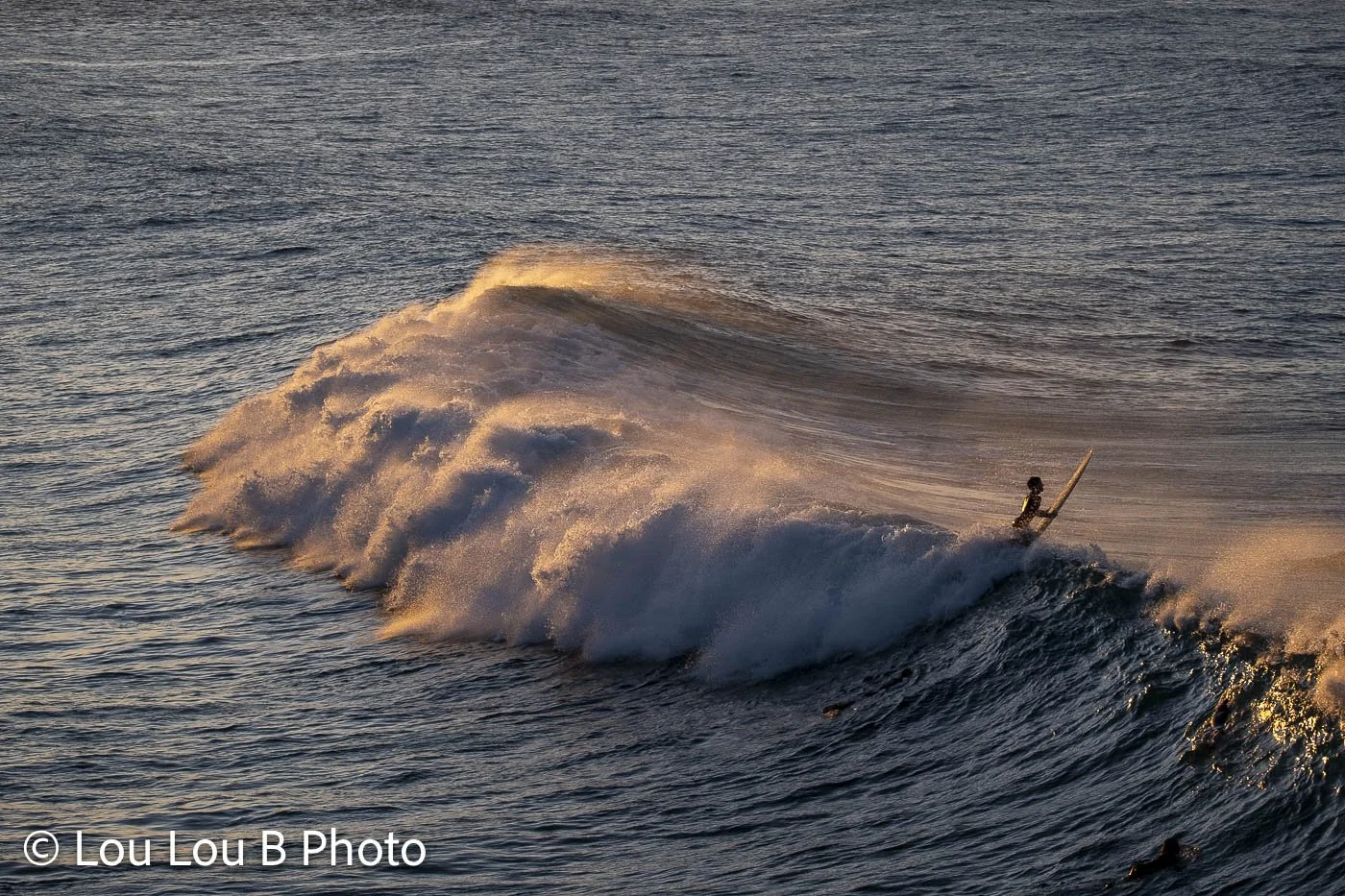 Surfer popping over a large breaking wave in Mount Maunganui Main Beach, surrounded by dramatic golden sea spray.