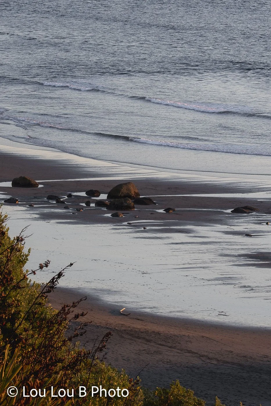 Elevated view of a quiet beach and silver-blue sea with rocks along the shoreline.
