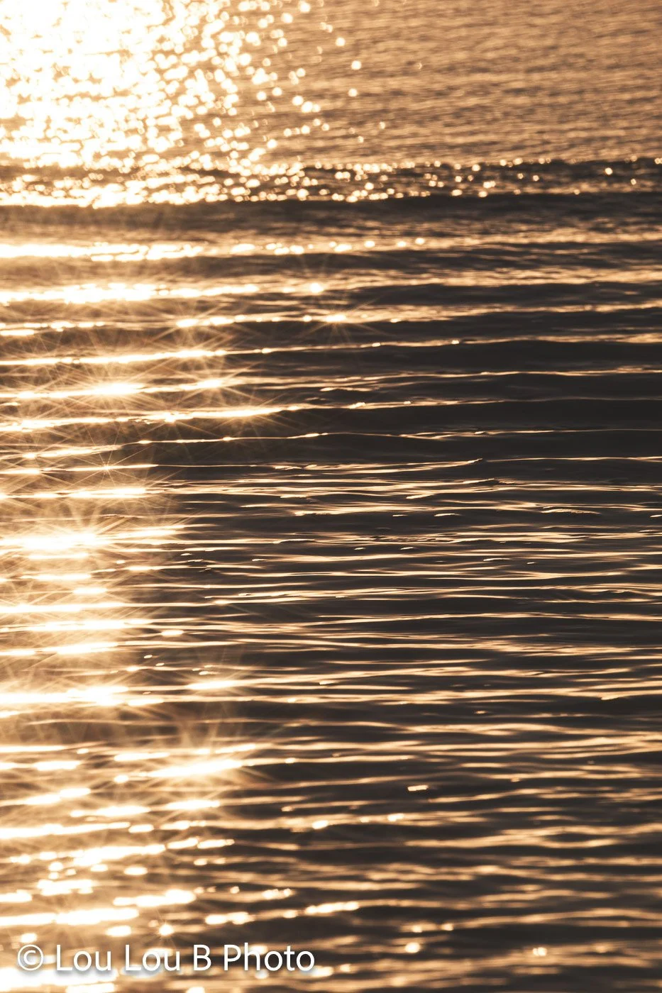 Golden sunlight reflecting across textured ocean water and parallel wave lines.